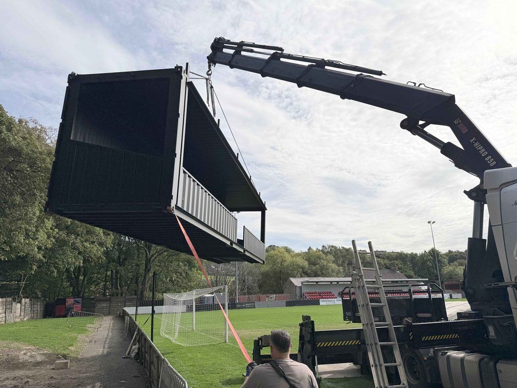 Shipping container spectator stand suspended in the air from the back of a lorry to be placed at Sheffield FC stadium.