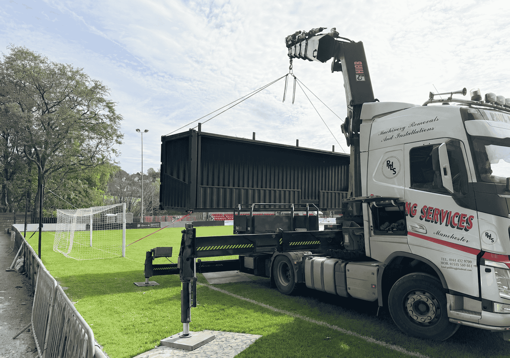 Shipping container spectator stand being lifted from a lorry at Sheffield FC stadium.